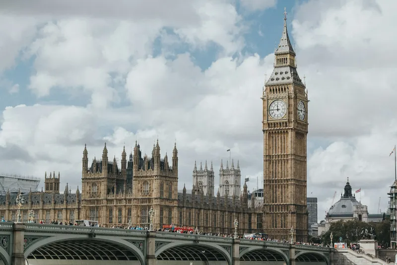 Iconic θέα του Big Ben και των Houses of Parliament στο Λονδίνο, με το Westminster Bridge γεμάτο κόσμο και διώροφα κόκκινα λεωφορεία να διασχίζουν τον Τάμεση.